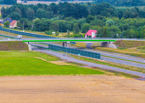 Aerial view of the S6 Expressway crossing over rural fields and green landscapes with sound barriers and nearby houses in Slupsk, Pomeranian Voivodeship, Poland.