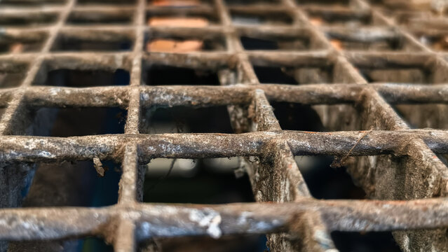 Close-up of a rusty metal sewer grate with a shallow depth of field, hinting at unseen depths below.
