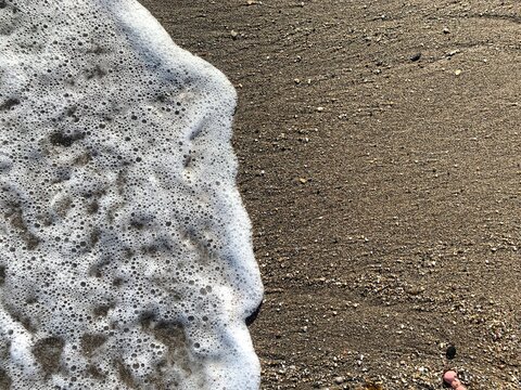 Ocean wave sea foam washing over wet beach sand background