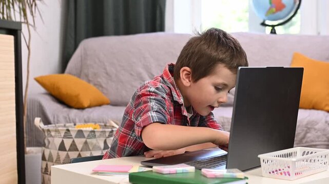 A 6-year-old boy is learning to type on a laptop and is sitting in the living room doing his homework.
