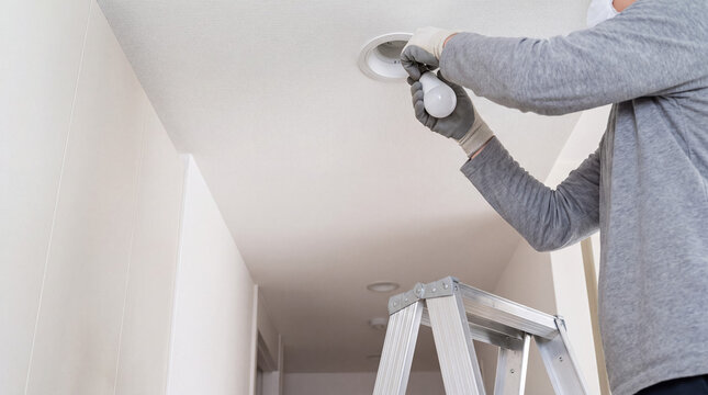 Person in gloves replacing an old light bulb with a new led in a ceiling fixture, standing on a ladder
