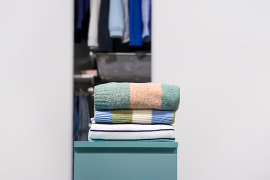 Folded pastel color striped woolen, warm sweaters with open wardrobe on light gray background. Concept of capsule wardrobe, minimalist clothing basics, seasonal changeover and organized home storage