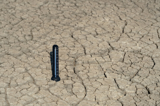 Thermometer standing on cracked dry soil during extreme heat, illustrating drought, high soil temperature, climate change, global warming and environmental crisis with copy space.