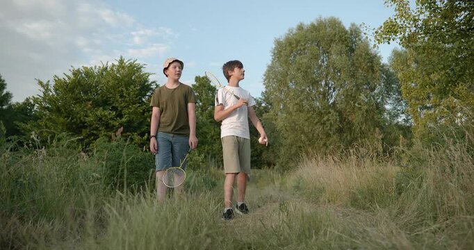 Two boys play badminton on nature. Teenagers spending time together. 4K 10-bit