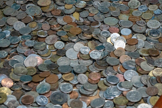 Variety of metal coins and currency of different sizes, colors, and face values ​​scattered across a flat surface. A mix of copper, brass, and silver colored metal coins.