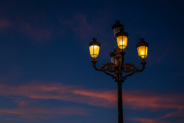 An old street lamp shines against a blue evening sky with pink clouds, Cadiz, Andalusia, Spain © Fotografierereien
