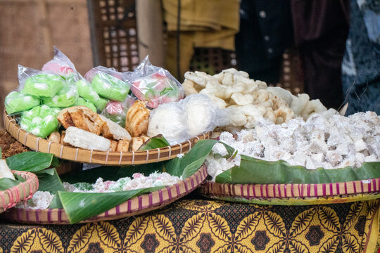 Colorful traditional Indonesian market snacks such as getuk, getuk lindri, and various other traditional treats served on woven bamboo trays or tampah lined with banana leaves. 
