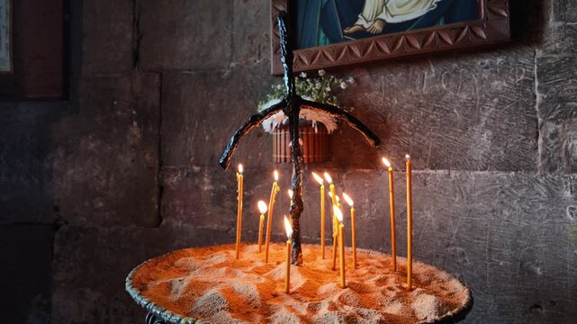 Burning wax candles in a traditional church candlestick standing against a stone wall, symbolizing faith, prayer, hope, spiritual ritual and religious devotion