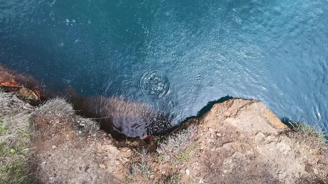 High angle shot of turquoise mineral water in a volcanic crater lake with rocky shore and shimmering sunlight on the surface, perfect for geological concepts or travel backgrounds