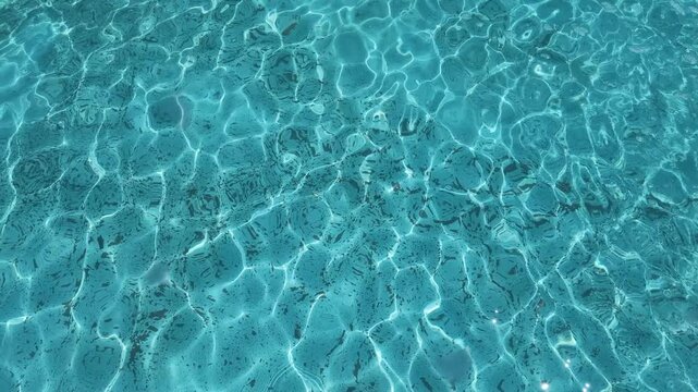 Sunlight caustic patterns rippling on the surface of turquoise blue water in a mosaic tiled swimming pool, perfect for summer background or travel design