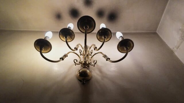 Vintage brass wall sconce with glowing bulbs and elegant ornate arms casting dramatic shadows on a textured wall, perfect for interior design, luxury home decor, architectural lighting, classic style
