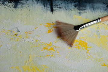 Artist brushes resting on a painted canvas surface with layered acrylic strokes, highlighting texture, color, and handmade artwork. © Amina