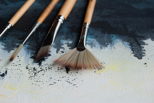 Painting brushes laid on canvas with colorful acrylic paint brushstrokes, showcasing an artistic workspace and creative process.