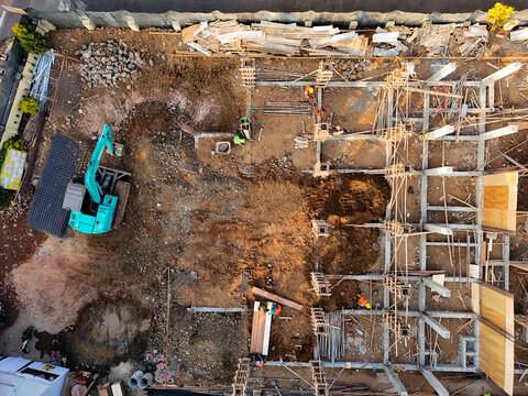 Aerial view of a construction site with workers, heavy equipment, and building foundations near Jalan Yos Sudarso in Kecamatan Purwokerto Barat, Jawa Tengah, Indonesia.