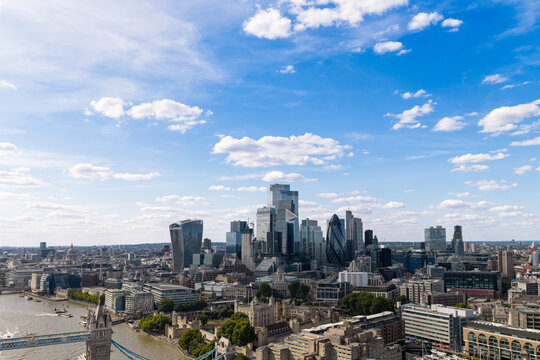 Aerial view of the London skyline featuring the Tower of London, Tower Bridge, and modern skyscrapers like The Gherkin and Walkie Talkie building under a blue sky United Kingdom.