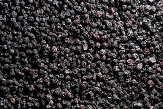 Top view macro background of dried organic aronia or blueberries. Closeup texture of dark wrinkled dried organic aronia chokeberries or wild blueberries scattered evenly in natural light with shadows