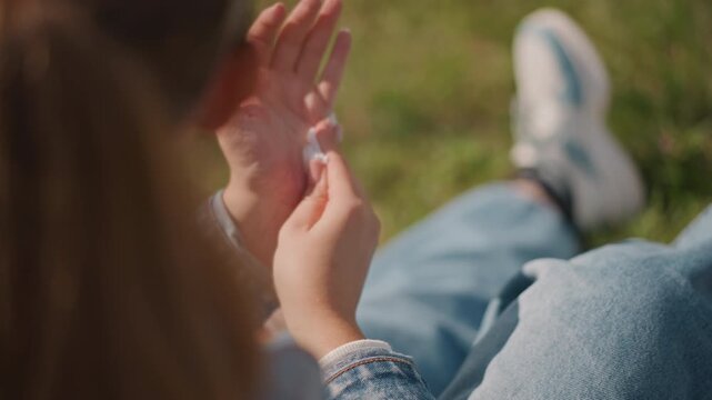 Female in denim cleans her hands thoroughly. Girl in outdoor sunlight carefully disinfects her hands. Young woman wearing denim jacket diligently refreshes her hands after enjoying snack outdoors