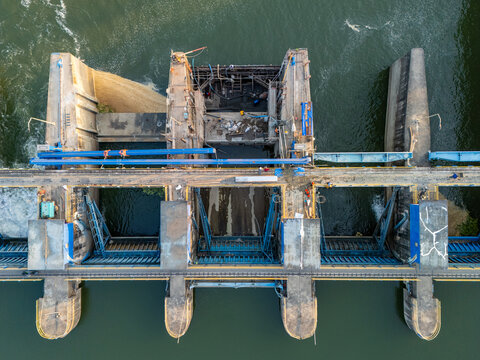 Aerial view of maintenance work at Bendung Gerak Serayu with workers on the concrete structure and flowing water in Kecamatan Rawalo, Jawa Tengah, Indonesia.