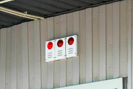 White wall-mounted units with bright red lenses and ventilation slots signal emergency status; corrugated metal backdrop and overhead conduit emphasize industrial safety environment.