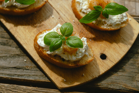 Bruschetta or crostini topped with cream cheese, shrimp and fresh basil. Tasty healthy snacks on wooden board.