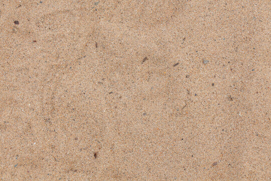 Uniform sandy surface in soft tan tones features delicate granules and sparse dark inclusions; natural texture conveys a quiet, undisturbed beach feel
