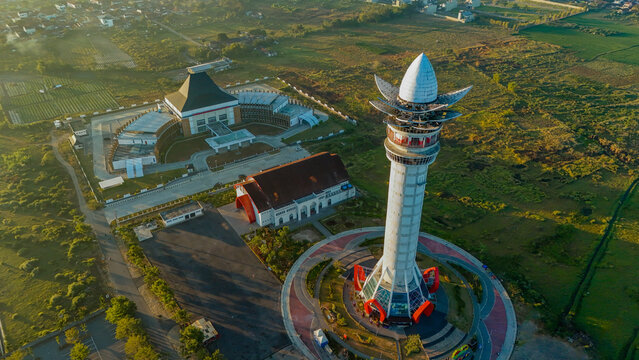 Aerial view of Menara Pandang Teratai surrounded by green fields and modern buildings in Kecamatan Purwokerto Timur, Jawa Tengah, Indonesia.