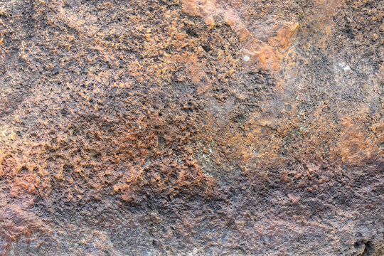 Earthy stone surface marked by iron oxide deposits; rusty streaks and granular textures reveal slow geological weathering