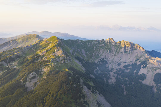 Aerial view of the rugged peaks and green slopes of Cerreto Laghi illuminated by golden hour light in the Apennine Mountains, Cerreto Laghi, Emilia-Romagna, Italy.
