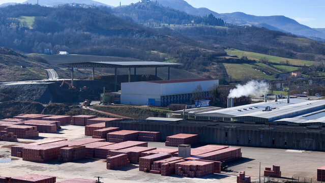 Aerial view of the brick factory and furnace with stacks of red building blocks and industrial buildings set against rolling hills in Lugagnano Val D'arda, Emilia-Romagna, Italy.