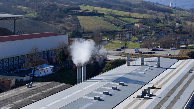 Aerial view of the brick factory and furnace with smoke rising from chimneys, set within the rural landscape of Lugagnano Val D'arda, Emilia-Romagna, Italy.