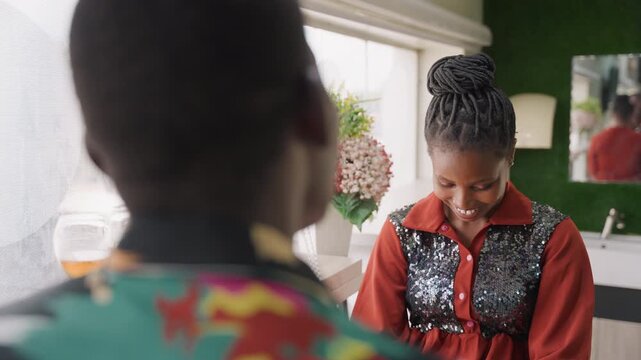 Black woman speaking softly to man across sunlit window, sincere expression with hands folded, intimate tone and reflective pause, floral decor, cozy apartment setting, emotional honesty, tender