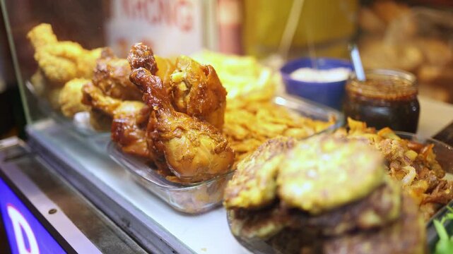 Assorted ingredients and fillings for banh mi sandwich displayed in glass showcase at street food stall in Nha Trang, Vietnam. Close up view of cooked chicken, patties, and sauces at local food market