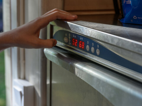 Hand adjusting modern stainless dishwasher control panel indoors.