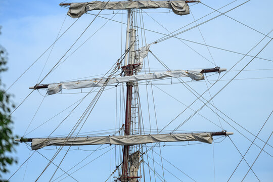Tall ship mast with folded sails and rigging lines.