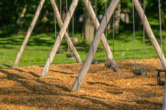 Empty playground swings hanging from rustic wooden frame.