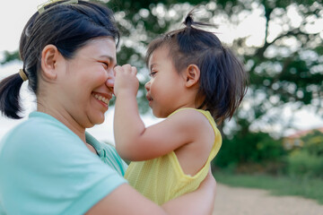 Fototapeta premium Little daughter hugging her mother outdoors and playing, expressing love, trust, family bonding, comfort, security, and precious parenting moments in a natural setting, Asian Thai people