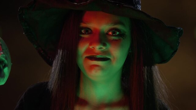 Portrait of teenage girl dressed as witch lowering skull to reveal her face and smiling into camera. Ideal for Halloween marketing campaigns and spooky seasonal promotions