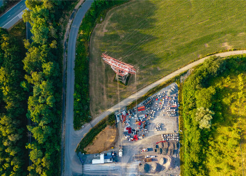 Aerial view of CCB Granulats Gaurain industrial site with a large power pylon, gravel piles, and surrounding green fields and trees in Tournai, Wallonia, Belgium.