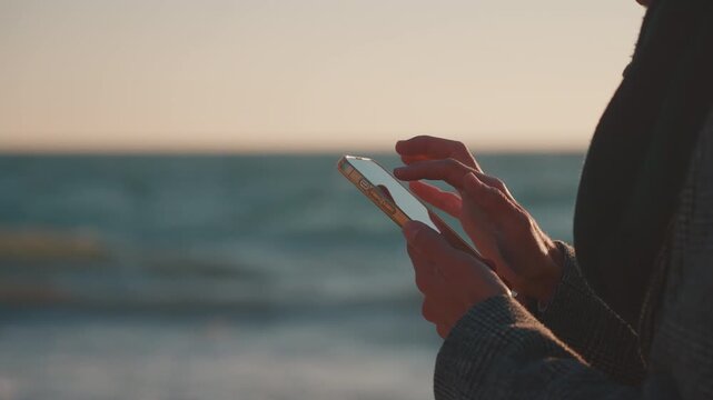 Close Up of Hands Scrolling on Smartphone by the Sea at Sunrise
