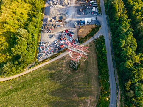 Aerial view of CCB Granulats Gaurain industrial site with gravel piles, heavy machinery, and a prominent electricity pylon surrounded by green fields and forest in Tournai, Wallonia, Belgium.
