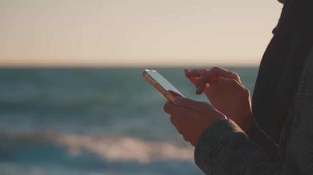 Hands Using a Smartphone with Sea in the Background at Sunrise