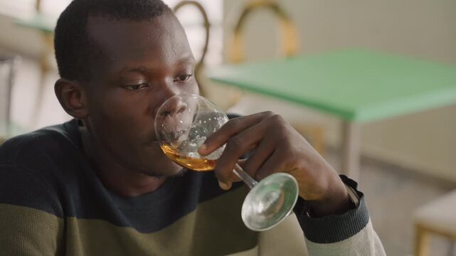 Thoughtful black man after sip staring into distance, contemplative pause and quiet tension, subtle worry and decision making, casual sweater and empty glass, late evening bistro atmosphere