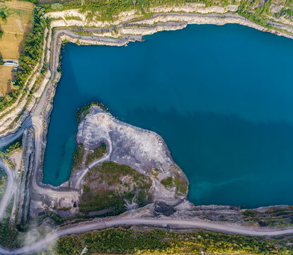 Aerial view of CCB Granulats Gaurain quarry featuring turquoise water, rocky cliffs, and surrounding greenery in Tournai, Wallonia, Belgium.