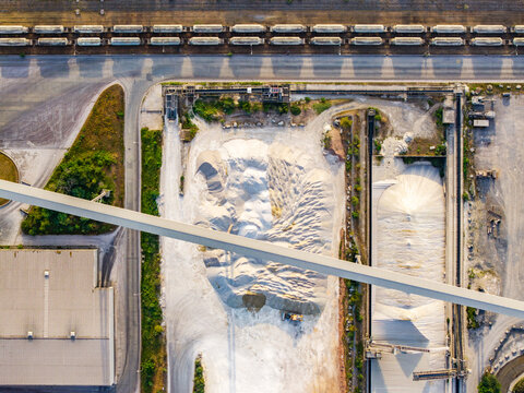 Aerial view of CCB Granulats Gaurain industrial site featuring large piles of gravel, conveyor belts, and adjacent railway tracks with freight cars in Tournai, Wallonia, Belgium.