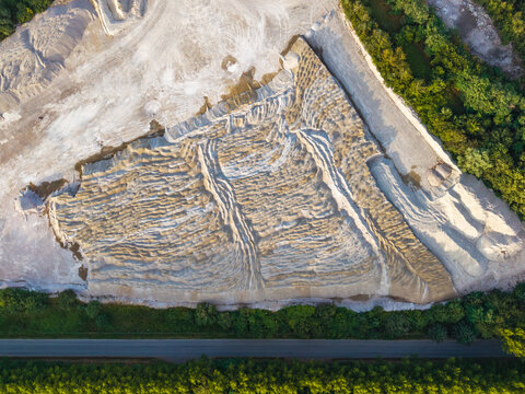 Aerial view of the CCB Granulats Gaurain quarry featuring textured gravel piles and industrial mining patterns surrounded by lush forest and a road in Tournai, Wallonia, Belgium.