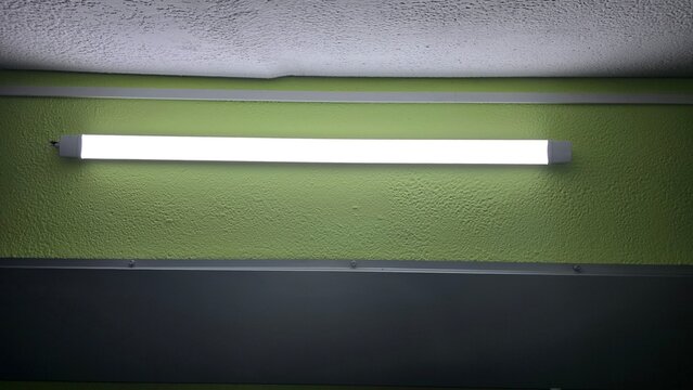Bright linear LED tube lamp mounted on green wall in basement shelter interior