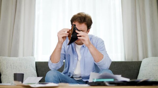 Stressed man holding empty wallet while looking at utility bill papers. High energy cost, financial crisis, and no money problem at home. High quality 4k footage