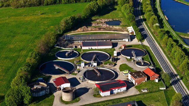 High-resolution aerial view of a modern wastewater treatment facility featuring multiple circular clarifiers, treatment basins, technical equipment, service buildings and supporting infrastructure.