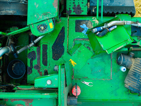 Aerial view of a broken combine harvester showing exposed mechanical parts, pipes, and maintenance tools on its green metal chassis in Kazupe, Dobele Municipality, Latvia.