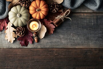 Fototapeta premium Cozy Autumn Flat Lay with Lit Candle, Mini Pumpkins, Pinecones, Cinnamon Sticks and Fallen Leaves on Rustic Wooden Background